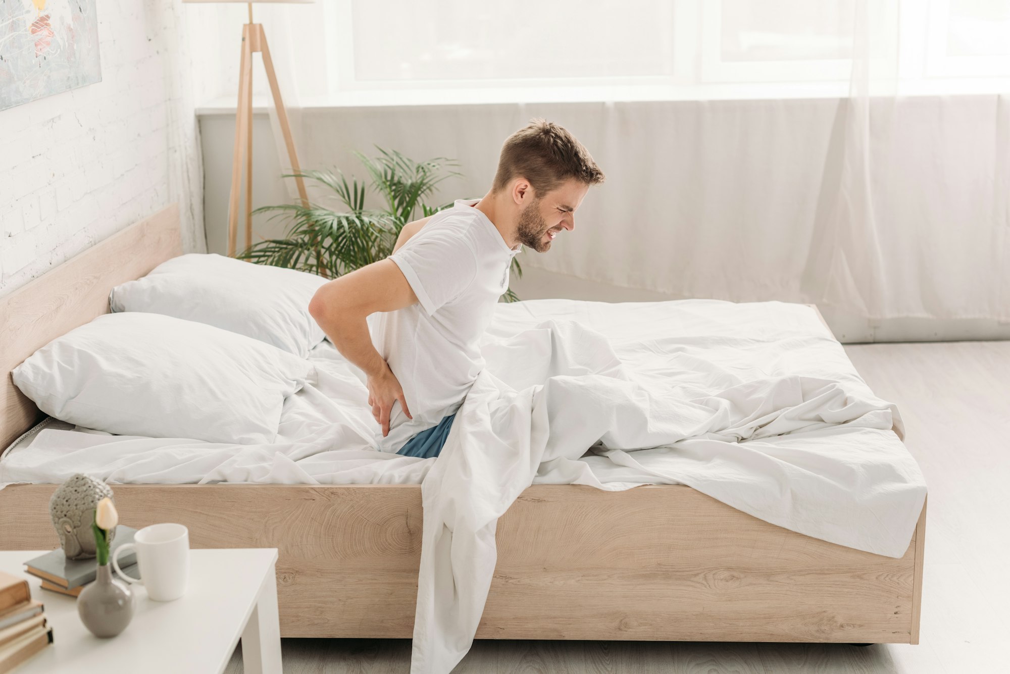 young man sitting in bed and suffering from pain in back